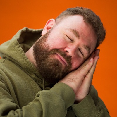 Logan Freedman, eyes closed with his head resting on his hands against an orange background
